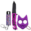 A self-defense keychain set featuring a black folding-blade knife with a bright magenta textured handle, a purple cat-shaped face shield, and a colorful glitter spray pepper spray canister with a silver keychain clasp.