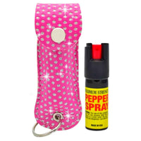 A pink rhinestone-covered pepper spray keychain case shown next to a black pepper spray canister with a red nozzle and yellow label, on a white background with decorative sparkle effects.